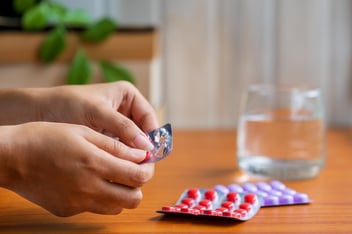 Person's hands removing a pill from a blister pack with a glass of water nearby