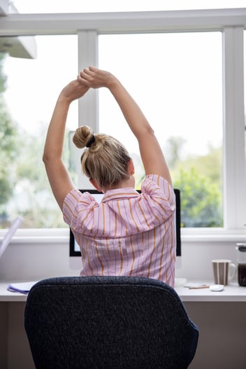 Female office worker at computer station, stretching arms while taking a break