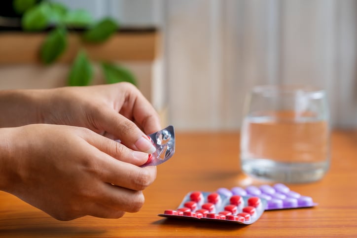 Person's hands removing a pill from a blister pack with a glass of water nearby
