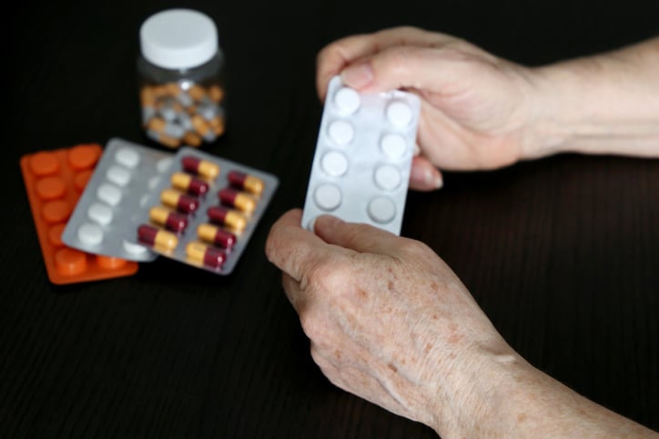 Hands of an elderly person holding blister pack of pills with other medications in background